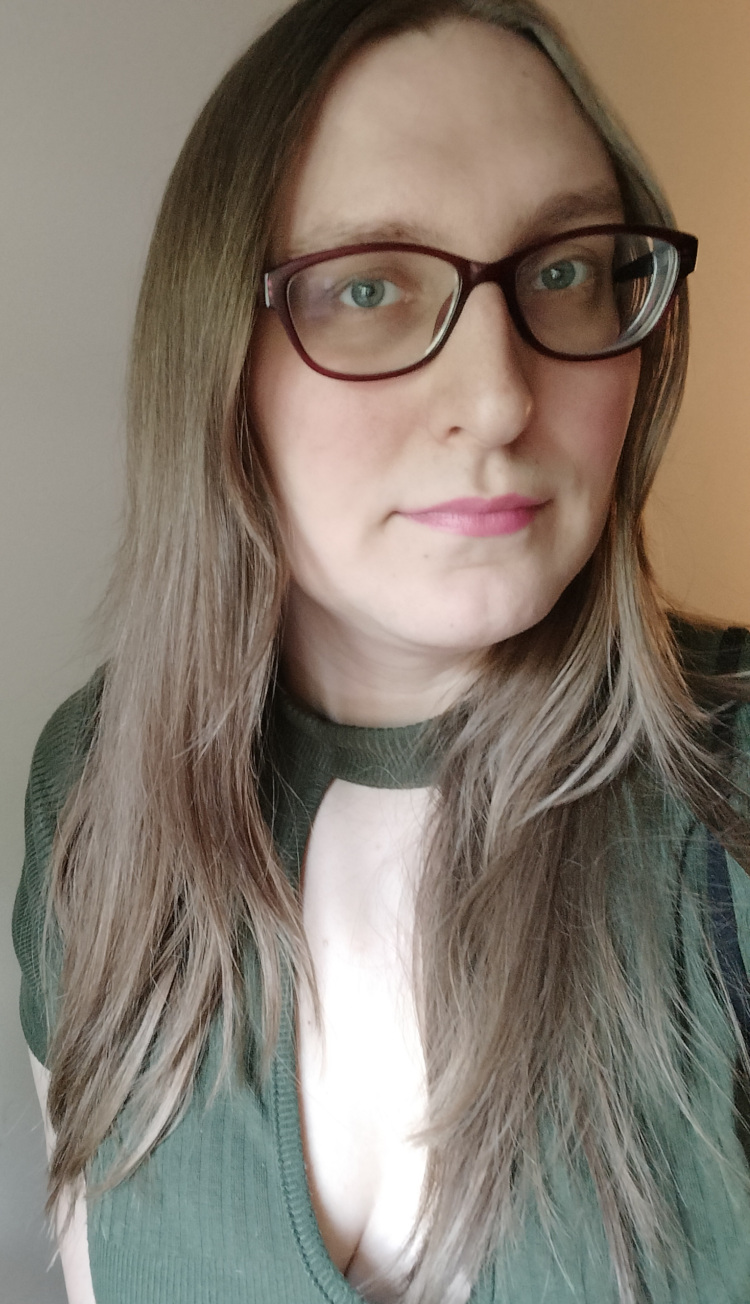 Headshot of the author, a white, blonde transgender woman wearing purple glasses and a green top.